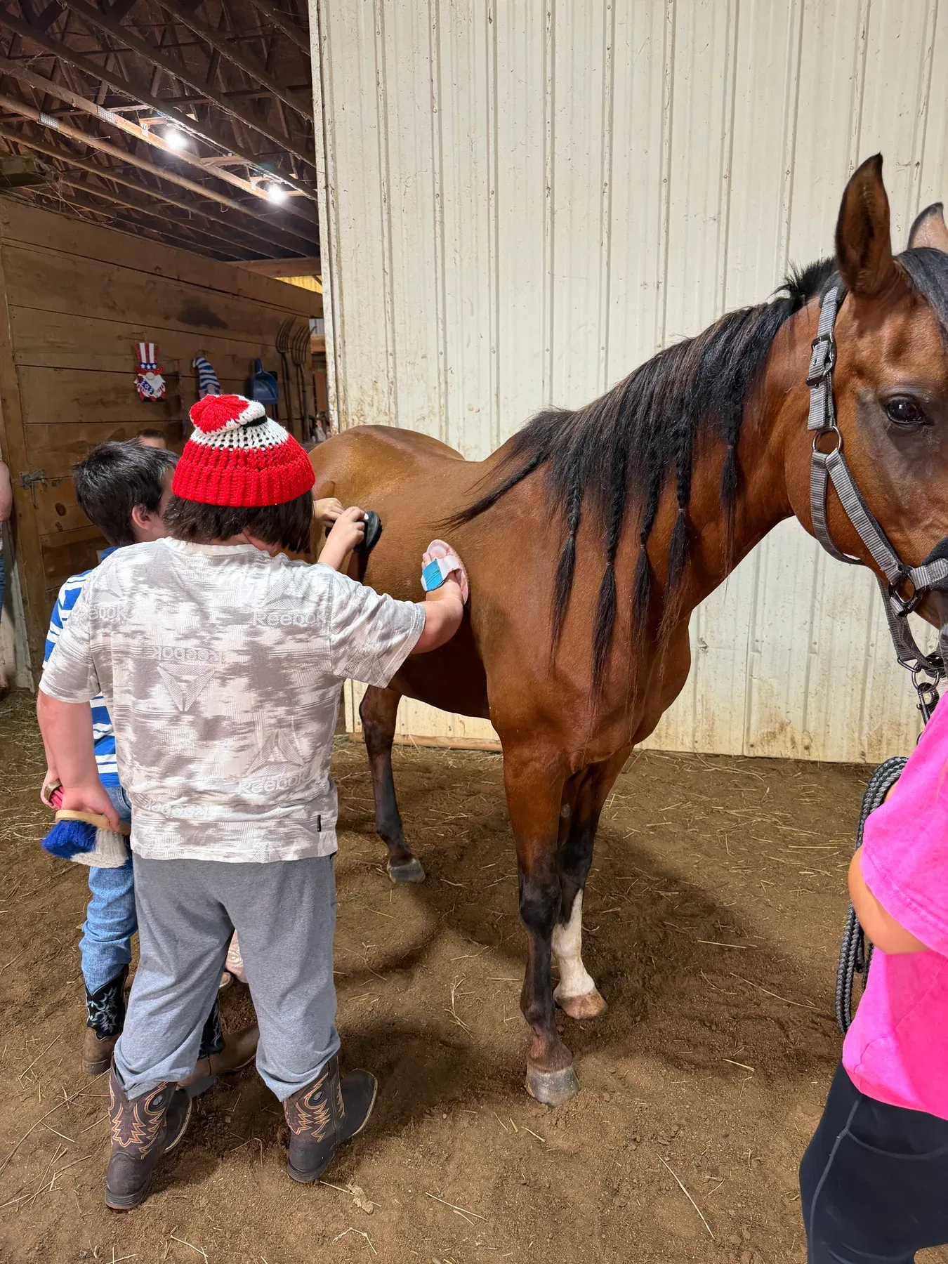 Young campers brushing a horse together inside the barn