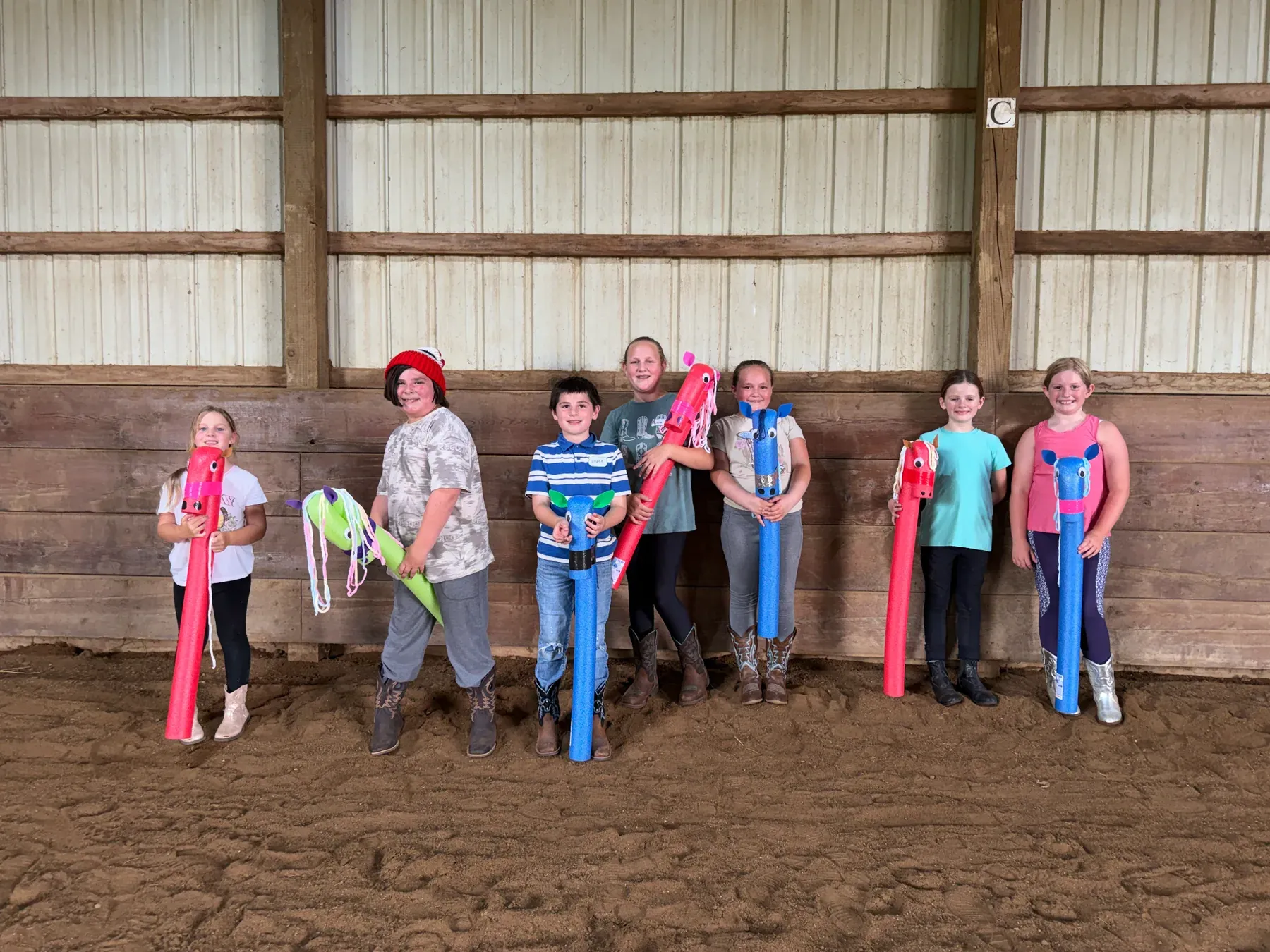 Young campers holding handmade hobby horses inside the MSB arena
