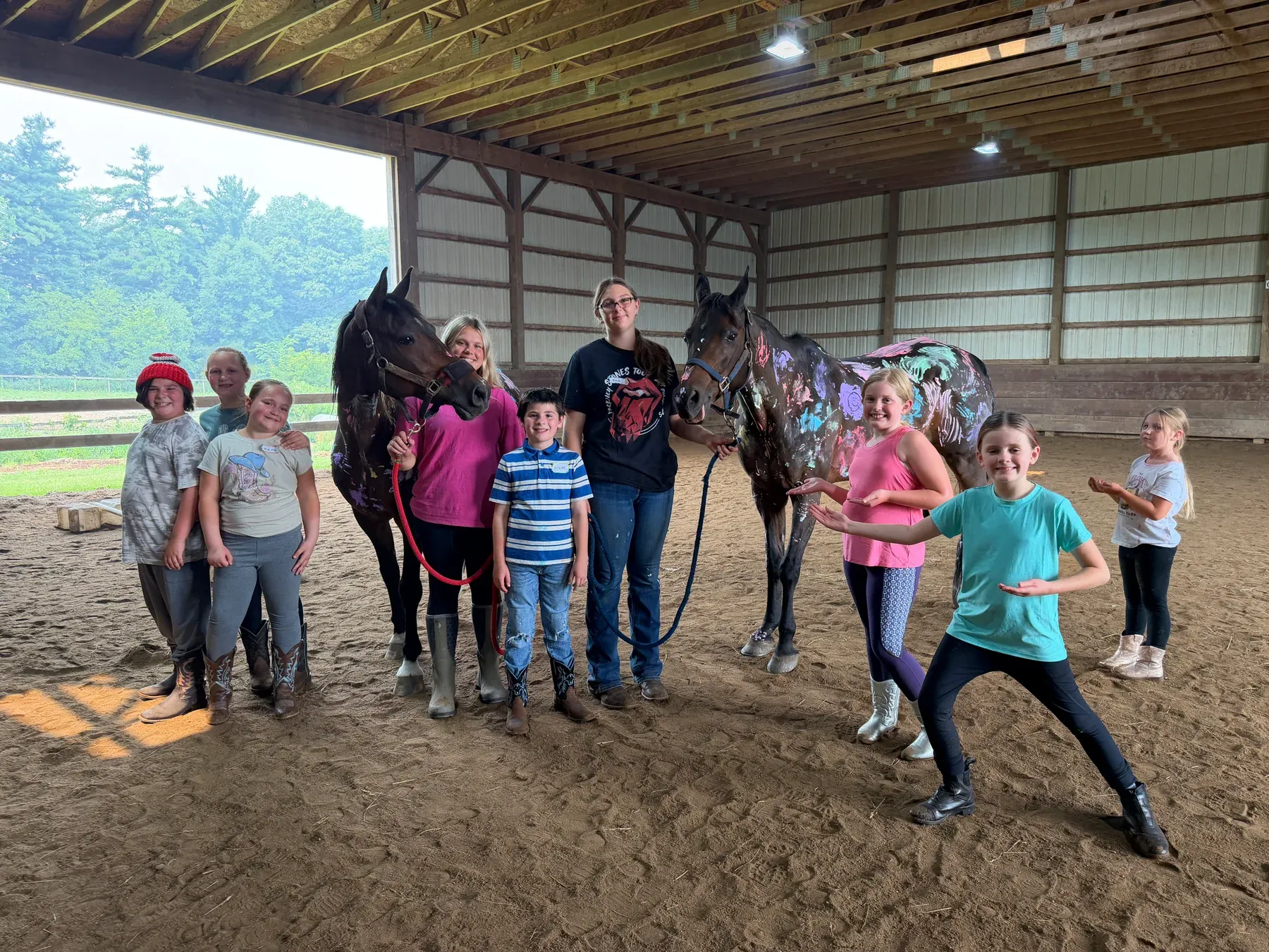 Campers posing with two horses decorated in colorful paint inside the arena